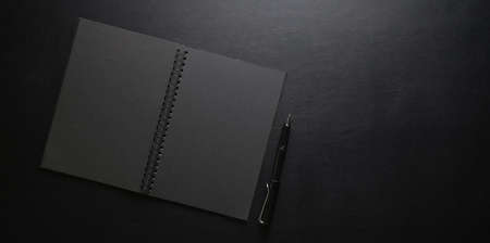 Top view of dark stylish workplace with notebook and pen on black leather desk backgroundの写真素材