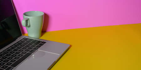 Modern colourful workplace with laptop computer and coffee cup on yellow desk and pink wall backgroundの写真素材