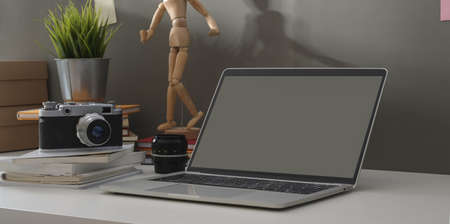 Minimal photographer workplace with open laptop and vintage camera with decorations on white table and grey wall backgroundの写真素材