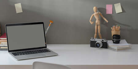 Comfortable workplace with open laptop and vintage camera with copy space on white table and grey wall backgroundの写真素材