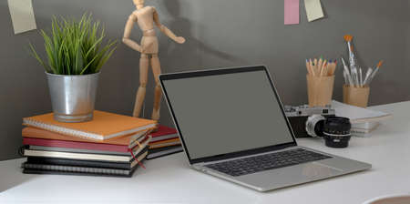 Trendy photographer workplace with open laptop and vintage camera with decorations on white table and grey wall backgroundの写真素材