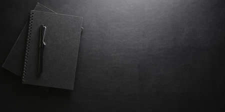 Dark stylish workplace with notebook and pen on black leather desk backgroundの写真素材