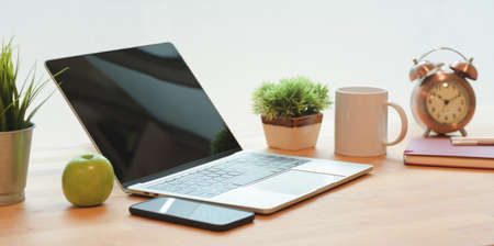 Open laptop computer with office supplies and smartphone on wooden table in comfortable workplaceの写真素材