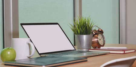 Open blank screen laptop computer with office supplies and smartphone on wooden table in comfortable workplaceの写真素材