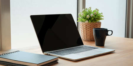 Open laptop computer with office supplies on wooden table in comfortable workplaceの写真素材