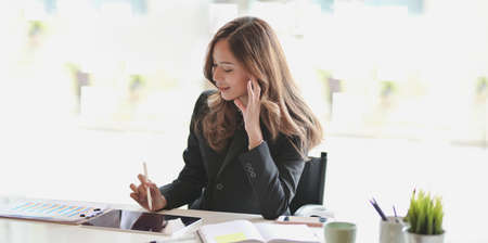 Beautiful Asian businesswoman working on her project while writing on tablet in modern office roomの写真素材
