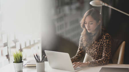 Beautiful Asian businesswoman working on her project while typing on laptop computer in modern workplaceの写真素材