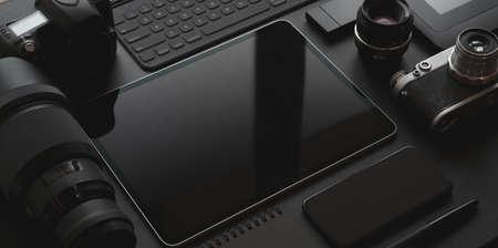 Dark trendy workplace with tablet, smartphone, camera and office supplies on black leather desk