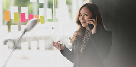 Attractive Asian businesswoman speaking on the phone with her customer in modern office roomの写真素材