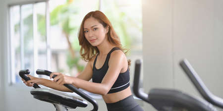 Beautiful Asian woman with slim body doing cardio workout on elliptical machine  in modern gymの写真素材