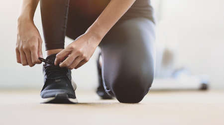Close-up view of young slim fitness girl doing shoelaces in the sport gym, preparing before runningの写真素材