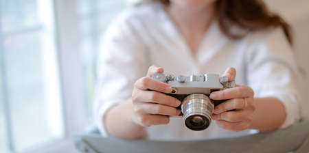Close-up view of young female photographer holding vintage camera in modern office roomの写真素材