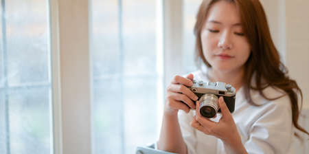 Beautiful young photographer checking her camera while working on her project in comfortable officeの写真素材