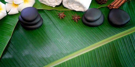 Spa therapy concept, Top view of black stones and towels for massages on green banana leaves backgroundの写真素材