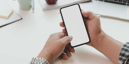 Close-up view of man holding blank screen smartphone in minimal office room with office suppliesの写真素材