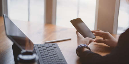 Close-up view of businesswoman touching smartphone in comfortable office room while working on her projectの写真素材