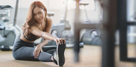 Beautiful Asian woman with tan and slim body stretching legs before exercise at the gymの写真素材