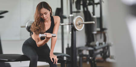 Beautiful asian athletic woman lifting dumbbell in weight training fitness gymの写真素材