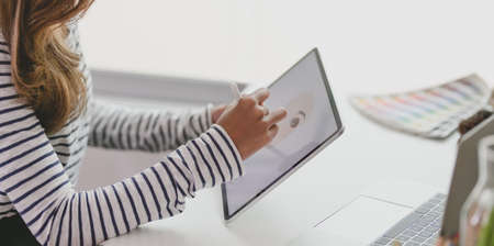 Cropped view of young graphic designer drawing her project on tablet in modern workplaceの写真素材