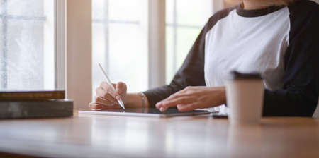Close-up view of female freelancer writing her idea concepts on tablet in comfortable working spaceの写真素材