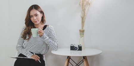 Professional designer working on her project while drinking a cup of coffee in modern workplaceの写真素材