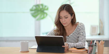 Professional female designer working on her project with tablet in comfortable workplace with decorationsの写真素材