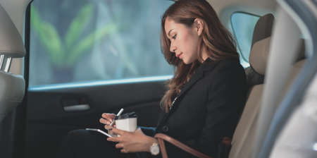 Beautiful professional asian businesswoman sitting on the back seat of the car, heading to the...