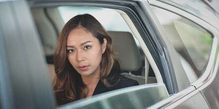 Close-up view of beautiful asian businesswoman sitting on the back seat of the modern car while looking at the cameraの写真素材