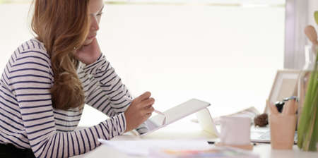 Passionate designer working on her project with tablet in modern workplace with office suppliesの写真素材