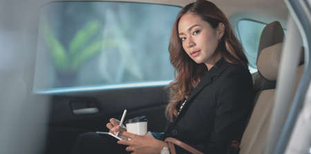 Professional asian businesswoman looking at the camera while sitting on the back seat of the modern carの写真素材