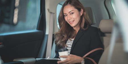 Attractive businesswoman working on the car with a cup of coffee while heading to the officeの写真素材