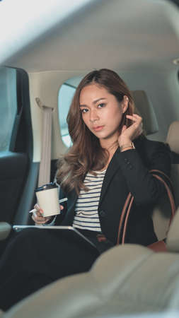 Professional asian businesswoman looking at the camera while sitting on the back seat of the modern carの写真素材
