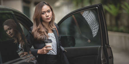 Portrait of beautiful businesswoman getting out of the modern luxury car while holding a coffee cupの写真素材