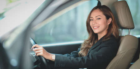 Beautiful professional asian businesswoman smiling at the camera while driving the car to the officeの写真素材