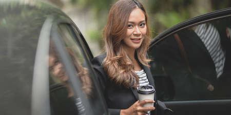 Beautiful professional businesswoman getting out of the modern luxury car while holding a coffee cupの写真素材
