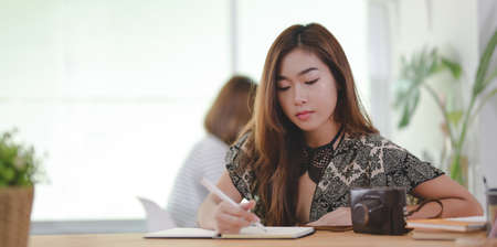 Cropped shot of professional female freelancer working on her project while writing on notebook in comfortable workplaceの写真素材