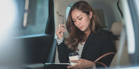 Young hard-working businesswoman working on the car with a cup of coffee while heading to the officeの写真素材