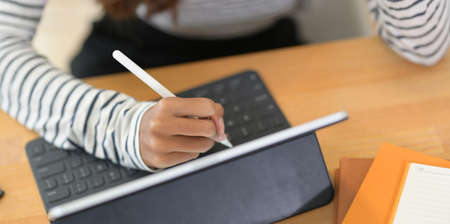 Cropped shot of passionate female designer working on her project while writing on tablet in modern workplaceの写真素材