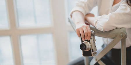 Cropped shot of young beautiful photographer holding camera while sitting on the chair in her modern workplaceの写真素材
