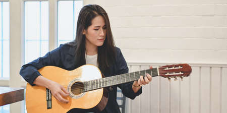 Beautiful middle-aged woman playing guitar in comfortable room during the relax timeの写真素材