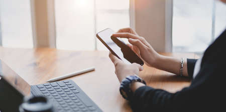 Close-up view of female freelancer searching information on smartphone in comfortable working spaceの写真素材