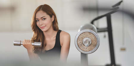 Fit asian athletic woman lifting weights inside the gym and smiling at the camera, muscular building conceptの写真素材