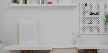 Minimal white workplace with mock up frame  and office supplies on white table and white wall backgroundの写真素材