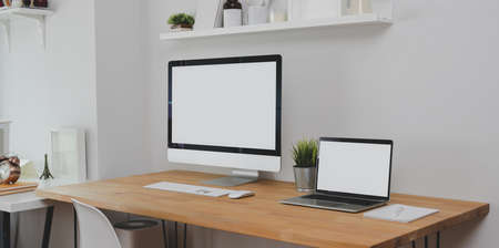 Trendy workplace with desktop computer, laptop computer and office supplies with decorations on wooden tableの写真素材