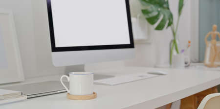 Modern workplace with desktop computer and blank screen laptop with copy space and office suppliesの写真素材