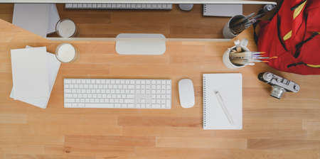 Top view of modern workplace with desktop computer and office supplies with red backpack on wooden tableの写真素材