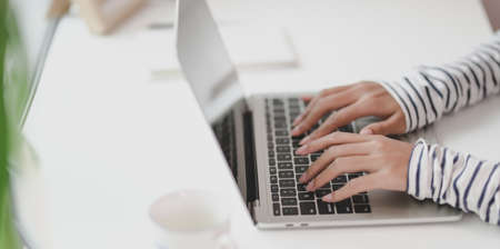 Close-up view of young professional designer working on her project while typing on laptop computerの写真素材