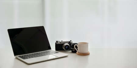 Open laptop computer with coffee cup and vintage camera on white table in comfortable workplaceの写真素材