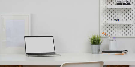 Open blank screen laptop computer with copy space and office supplies in minimal white office roomの写真素材