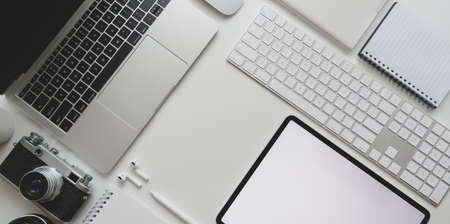 Top view of modern workplace with laptop computer, camera, tablet, office supplies on white desk background with copy spaceの写真素材
